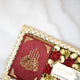 Red book with gold design on a white surface with flowers and a box.