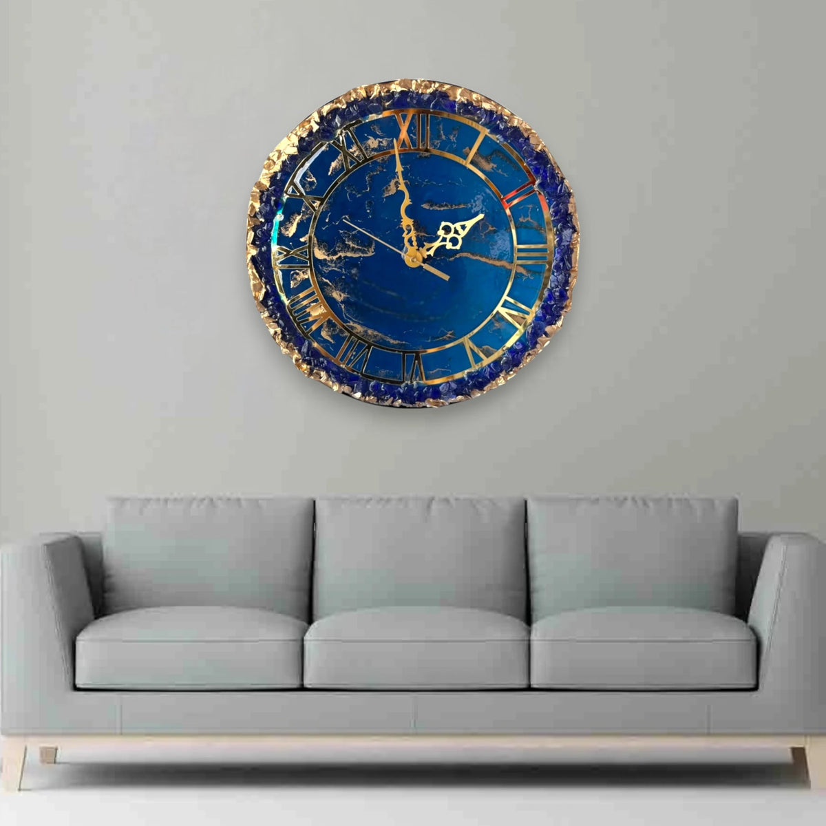 Eternal Blue Elegance Wall Clock with gold detailing and resin finish, displayed above a grey sofa in a modern living room setting.