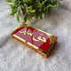 Angled view of red and gold Haqq Mehr envelope with ornate border, used for ceremonial gifting during weddings and Nikah.