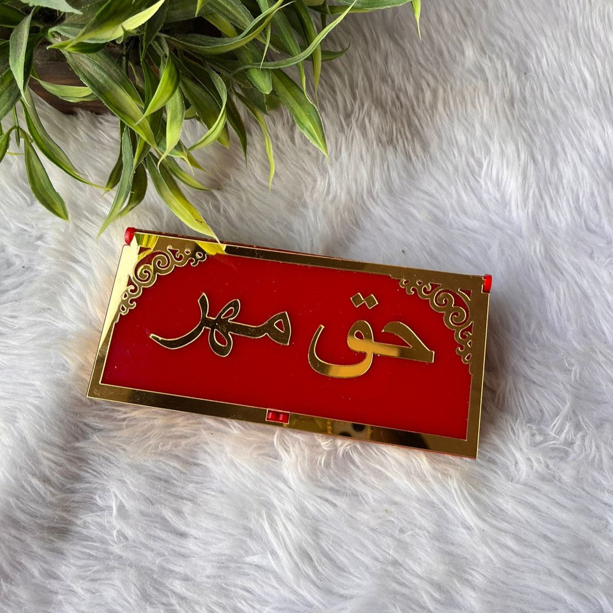 Red Haqq Mehr envelope with gold detailing placed on white fur background. A traditional and decorative Nikah gift box.