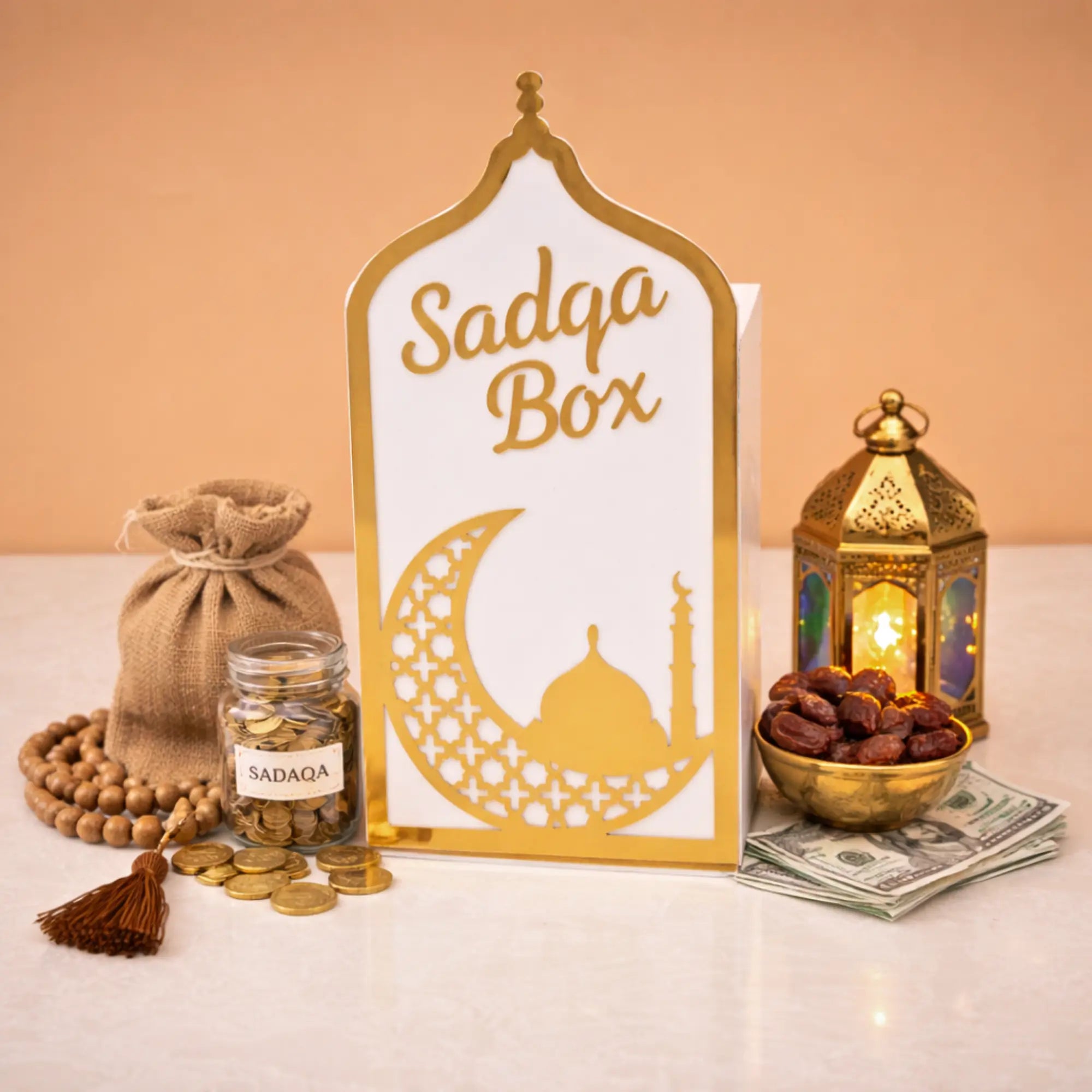 White Sadaqah Box with gold detailing, surrounded by coins, dates, and lantern, ideal for housewarming and Ramadan gifts in Religious Items.