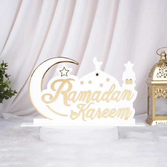 Decorative sign with 'Ramadan Kareem' text on a white background with a gold lantern and green plant.