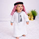 Baby boy wearing traditional white thobe with embroidery, standing on white fluffy rug