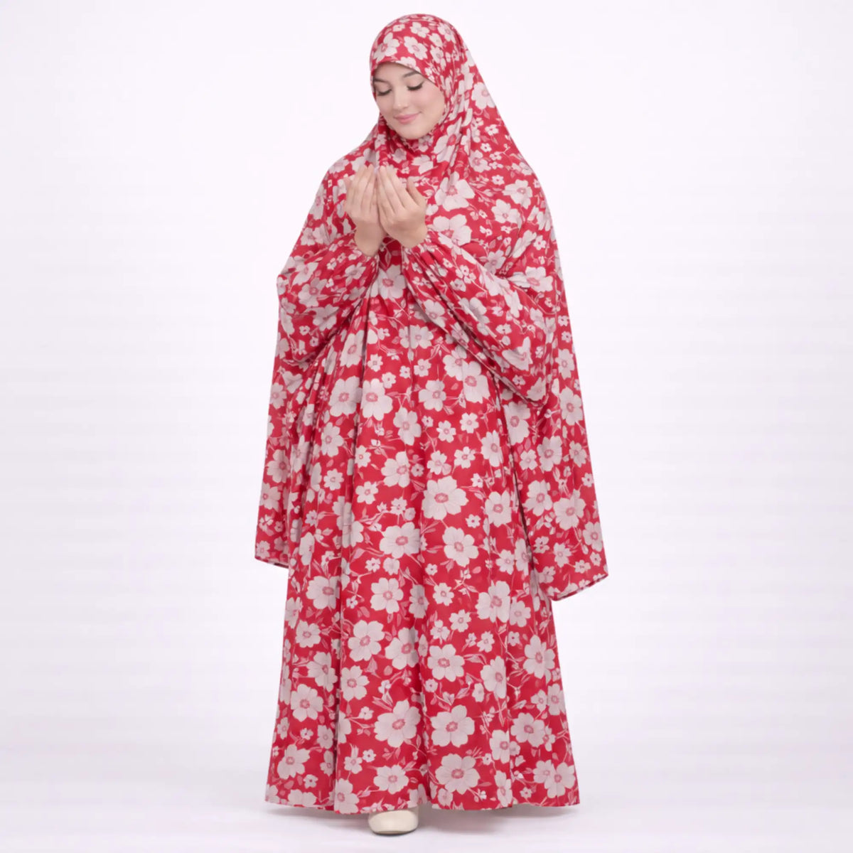 A woman with her hands raised in prayer, wearing a full-length red prayer dress covered in a light pink and white floral print.