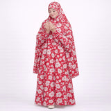 A woman with her hands raised in prayer, wearing a full-length red prayer dress covered in a light pink and white floral print.