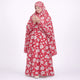 A woman with her hands raised in prayer, wearing a full-length red prayer dress covered in a light pink and white floral print.