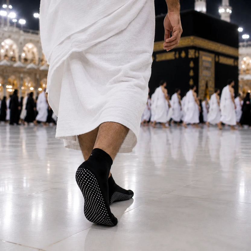 A person walking in a grand mosque courtyard wearing black non-slip socks with textured grip dots, with the Kaaba and other pilgrims blurred in the background. Main image