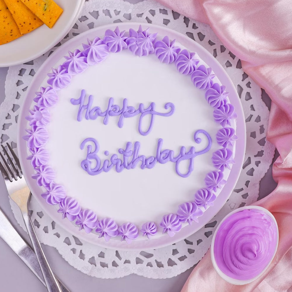 Top view of Floral Vanilla Cream Cake featuring purple floral accents and 'Happy Birthday' icing text, perfect for elegant celebrations.