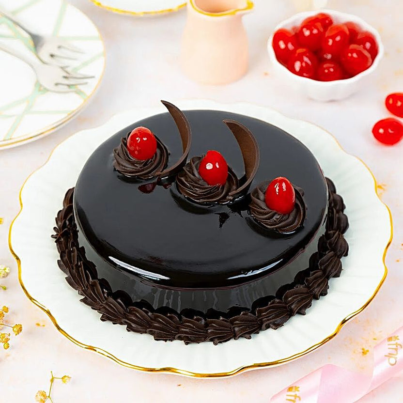 Yummylicious Chocolate Cake - Order Dessert Online | Rich Indulgence, glossy round chocolate cake topped with cherries and chocolate swirls on a white plate. Main image