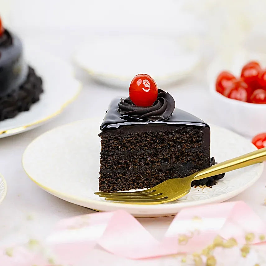 Yummylicious Chocolate Cake - Order Dessert Online | Rich Indulgence, moist chocolate cake slice with rich layers, glossy topping, and cherry garnish on a dessert plate.