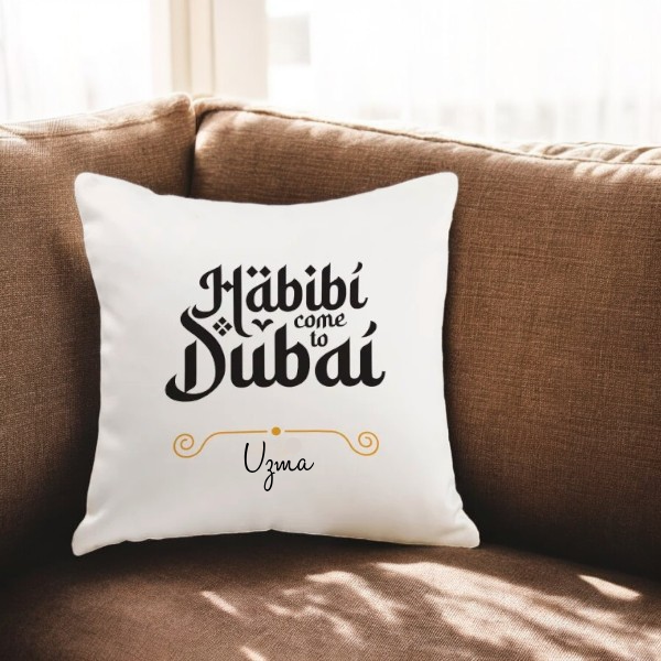 Habibi Dubai Cushion - Personalized with name Uzma on white fabric, placed on a brown sofa. Ideal custom gift for home decor or special occasions.