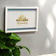Mashallah Wooden Home Decor Frame in A3 size mounted on a wall near green indoor plant, showcasing gold Islamic calligraphy and handmade detailing.
