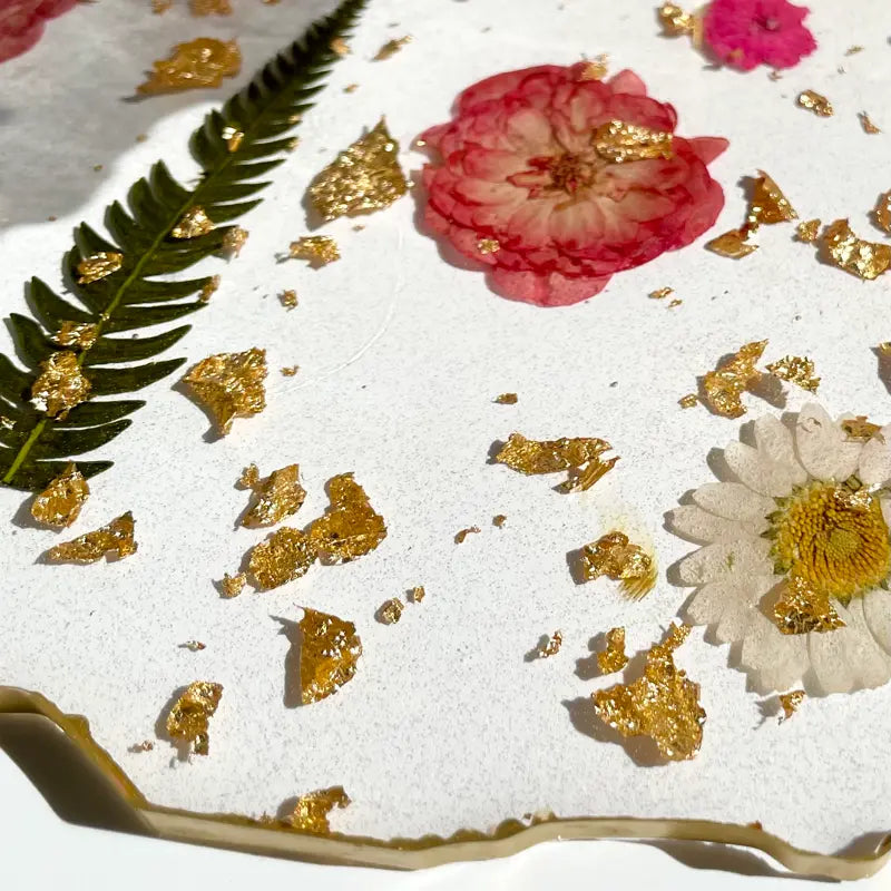 Close-up of a dessert with gold leaf, pink and white flowers on a white surface.