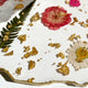 Close-up of a dessert with gold leaf, pink and white flowers on a white surface.
