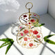 Three-tiered decorative tray with floral design on a white surface with fern leaves.