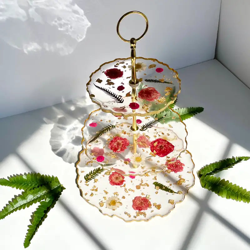 Three-tiered decorative tray with floral design on a white surface with fern leaves. Main image