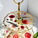 Two-tiered cake stand with floral design and gold accents on a white background