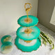 Three-tiered turquoise serving tray with gold accents on a marble surface.