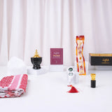 A front-facing display of the Son of the Ummah Men's Gift Hamper items arranged on a white surface against a white curtain. The collection features a folded red and white checkered ghutra, a white prayer cap, a black and gold bakhoor burner, a maroon 'Fortress of the Muslim' book, a packaged miswak, a white digital tasbeeh with a compass and red tassel, a small attar bottle, and a black gift box with the Hadiyah logo.