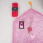 Top-down view of the Little Soul Essentials Hamper contents laid flat on a light surface. It features a light pink quilted kids' prayer mat, a pink digital tasbeeh on a printed card, a matching pink 33-bead tasbeeh with a large agate stone and tassel, and a bright pink rolled prayer makhana secured with a black Hadiyah band.