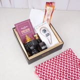 An overhead view of the Son of the Ummah Men's Gift Hamper. A black gift box with gold inner lining contains a white prayer cap, a packaged miswak, a maroon 'Fortress of the Muslim' book, a boxed digital tasbeeh with a compass, a black and gold bakhoor burner, a small black jar of bakhoor, and an attar bottle nestled inside. A red and white checkered ghutra rests on the white surface outside the bottom right corner of the box.