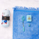 A blue Women's Namaz Essentials Hamper displayed as a flat lay, featuring a rolled floral prayer dress, a plush blue velvet prayer mat, a light blue mini velvet Quran box, blue tasbeeh beads, and a digital counter.